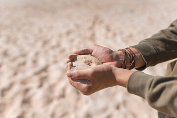 Man holding white sand in his hands. Male palms with the sand on the beach.