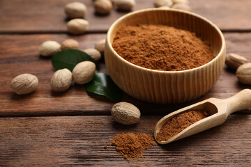 Nutmeg powder and seeds with green leaves on wooden table