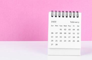 February 2022 desk calendar on white table with pink background.