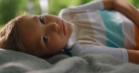 Portrait of tranquil boy lying on blanket closeup. Blond kid looking on camera.