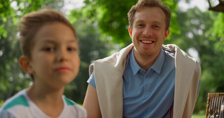 Winking happy man laughing on camera close up. Father seat with son on picnic.