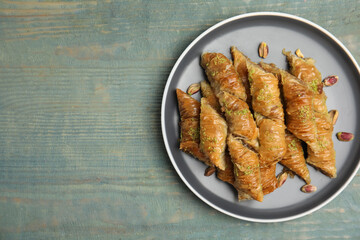 Delicious baklava with pistachio nuts on light blue wooden table, top view. Space for text