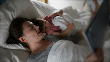 Mother lying in bed with child reading a bedtime story before sleep