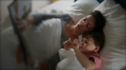 Mother lying in bed with child reading a bedtime story before sleep