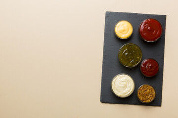 Different tasty sauces in bowls on plate on colored background. top view