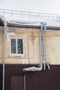 Two curved metal exhaust pipes on the wall of the house. There is white snow on the surface. Against the background of a gray sky. Cloudy winter day, soft light.