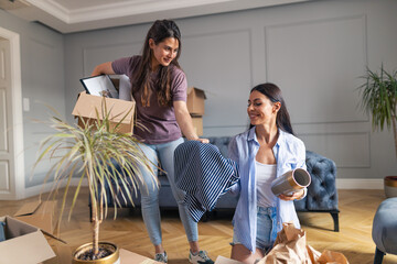 Lesbian couple unpacking personal belongings in their new apartment. - obrazy, fototapety, plakaty