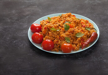 Jollof rice, tomatoes and hot peppers on a blue plate on a black background. National cuisine of Africa.