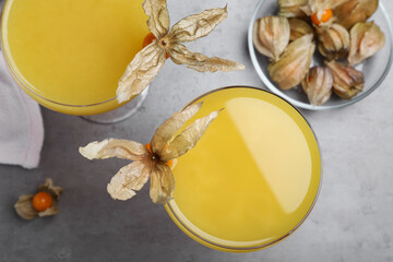 Tasty cocktail decorated with physalis fruits on grey table, flat lay