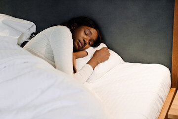Black young woman sleeping on white bed linen at home