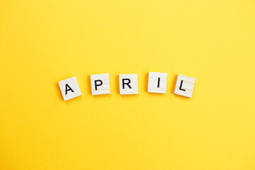 inscription April made by wooden cubes on a yellow background.