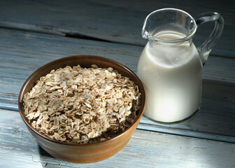 Oatmeal in a wooden bowl, oatmeal and cup of milk on the  table. Healthy eating