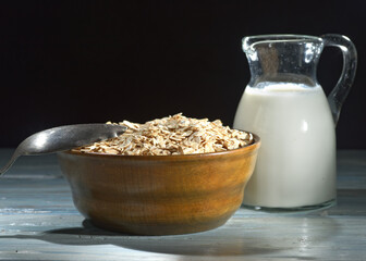 Oatmeal in a wooden bowl, oatmeal and cup of milk on the  table. Healthy eating