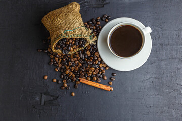 Coffee beans in brown sack bag with coffee cup on black background.