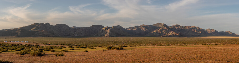 Ein Bergpanorama mit einer steppenartigen Landschaft, gelben Sand sowie einem grün bewachsenen Plateau am Rande der Wüste Gobi