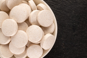 Several medical tablets with a ceramic white saucer on a slate stone, macro, top view.