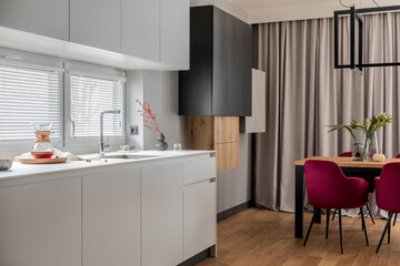 Stylish composition of kitchen and dining room open space interior. Minimalist ergonomic kitchen space. Velvet chairs, wooden table and personal accessories in the modern dining room. Template.