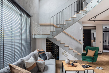 Stylish composition of stairs in living room interior. Grey sofa, green velvet armchair, coffee...
