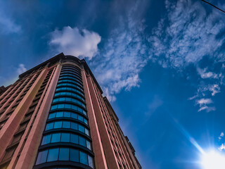Urban landscape with multi-storey modern skyscraper against cloudy blue  sky. Business center cityscape. Office building architecture.