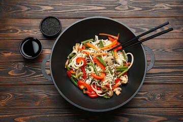 Stir fried noodles with mushrooms and vegetables in wok on wooden table, flat lay