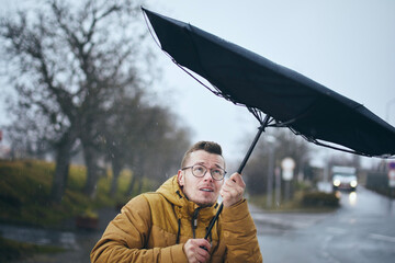 Man holding broken umbrella in strong wind during gloomy rainy day. Themes weather, meteorogy and climate changes.. - obrazy, fototapety, plakaty