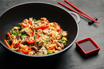 Stir fried noodles with mushrooms, shrimps and vegetables in wok on black table, closeup