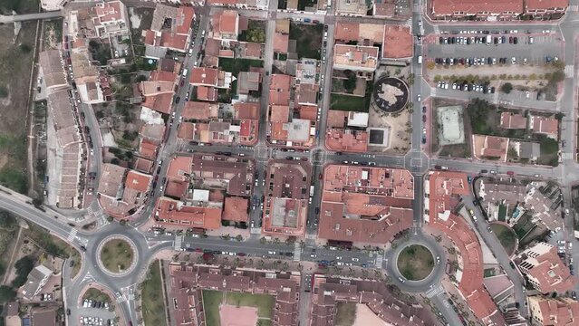A breathtaking aerial view of a city in Spain: tiled rooftops of houses are seen from the air together with streets, intersections, and squares, where cars are parked