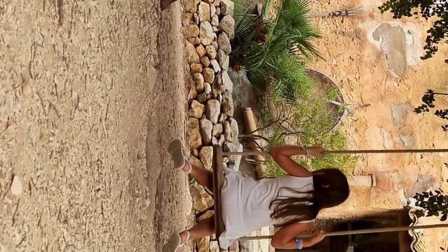 Back view of adorable little girl swinging on tree swing, Italy. Slow-motion. VERTICAL format
