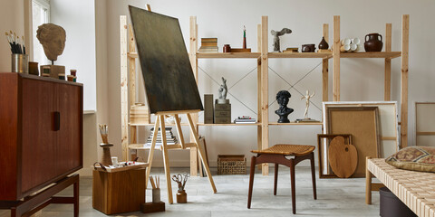 Unique artist workspace interior with stylish teak commode, wooden easel, bookcase, artworks, painting accessories, decoration and elegant personal stuff. Modern work room for artist. Template.