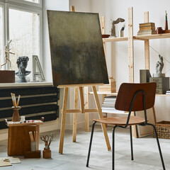 Unique artist workspace interior with stylish teak commode, wooden easel, bookcase, artworks, painting accessories, decoration and elegant personal stuff. Modern work room for artist. Template.