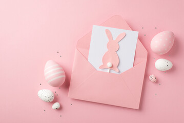 Top view photo of easter decorations open pink envelope with paper card and easter bunny silhouette confetti pink and white easter eggs on isolated pastel pink background