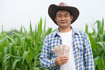Handsome Asian  male farmer wears hat, holds Thai banknote money at maize field. Concept : Farmer...