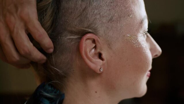 A close-up of a woman's head is shaved bald with a hair clipper indoor.