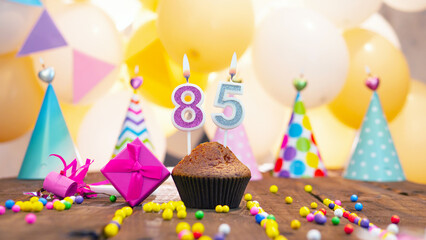 Happy birthday with a number of candles for eighty-five years on the background of balloons. A...
