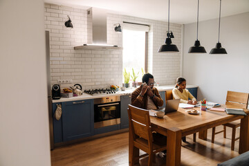Black man talking on cellphone while his daughter doing homework