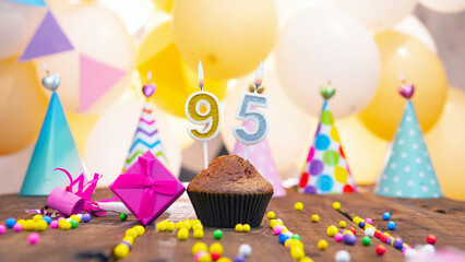 Happy birthday with a number of candles for ninety-five years on the background of balloons. A festive muffin with burning candles and a pink gift box for a woman. Happy birthday for 95 years
