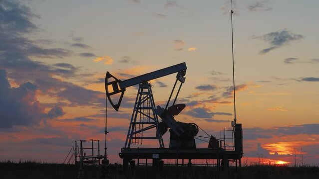 Silhouette working oil pump in deserted district at sunset. Oil drill rig and pump jack. Oil drilling derricks at desert oilfield for fossil fuels output and crude oil production from the ground.