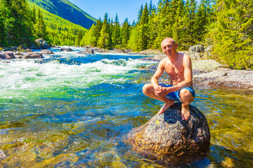 Young man on rock in river Rjukandefossen waterfall Hemsedal Norway.