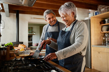 Elderly multi-ethnic couple laughing together in the kitchen. Happily retired and cooking breakfast with each other. - 487803669