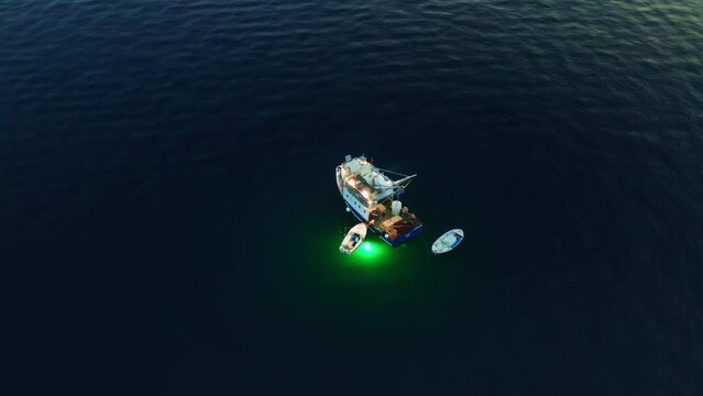 Evening fishing in Adriatic sea from vessel and small boats. Bright green lantern illuminates dark blue water to attract fish at darkness. Aerial view