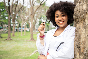 Portrait of beautiful young scientist holds a magnifying glass to use to explore and find plant and...