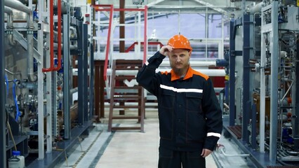 A plant worker straightens an orange work helmet, a process equipment operator stands in a gas compression workshop. Oil and gas or chemical industry. dynamic zoom
