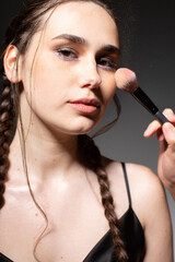 Portrait of making makeup young european woman with two braids with brown eyes isolated on dark grey