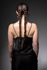Turned back young european woman with two braids isolated on dark grey in total black outfit