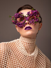Woman with eye mask made of small flowers with purple lips portrait isolated on grey brown