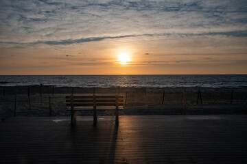 Naklejka na ściany i meble Sunrise and a bench on the boardwalk by the beach