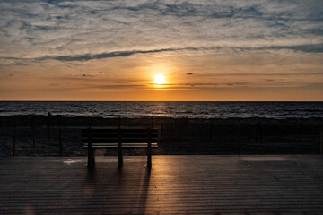 Obraz premium Sunrise and a bench on the boardwalk by the beach