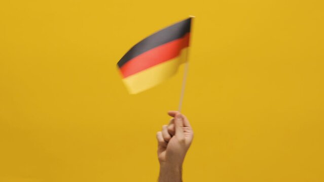 Man's hand waving flag of Germany. Human hand holding Germany flag on yellow background.