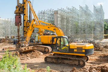 A large yellow excavator with a front bucket collects earth at a construction site during construction