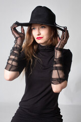 White young european woman in total black isolated on grey holding her hat by fingers